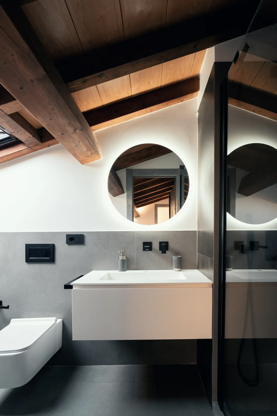 Bagno in mansarda con travi a vista, specchio tondo retroilluminato e mobile sospeso