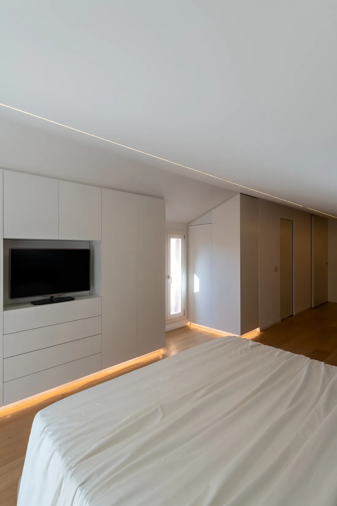 Camera da letto in mansarda con armadiature su misura e illuminazione LED a pavimento