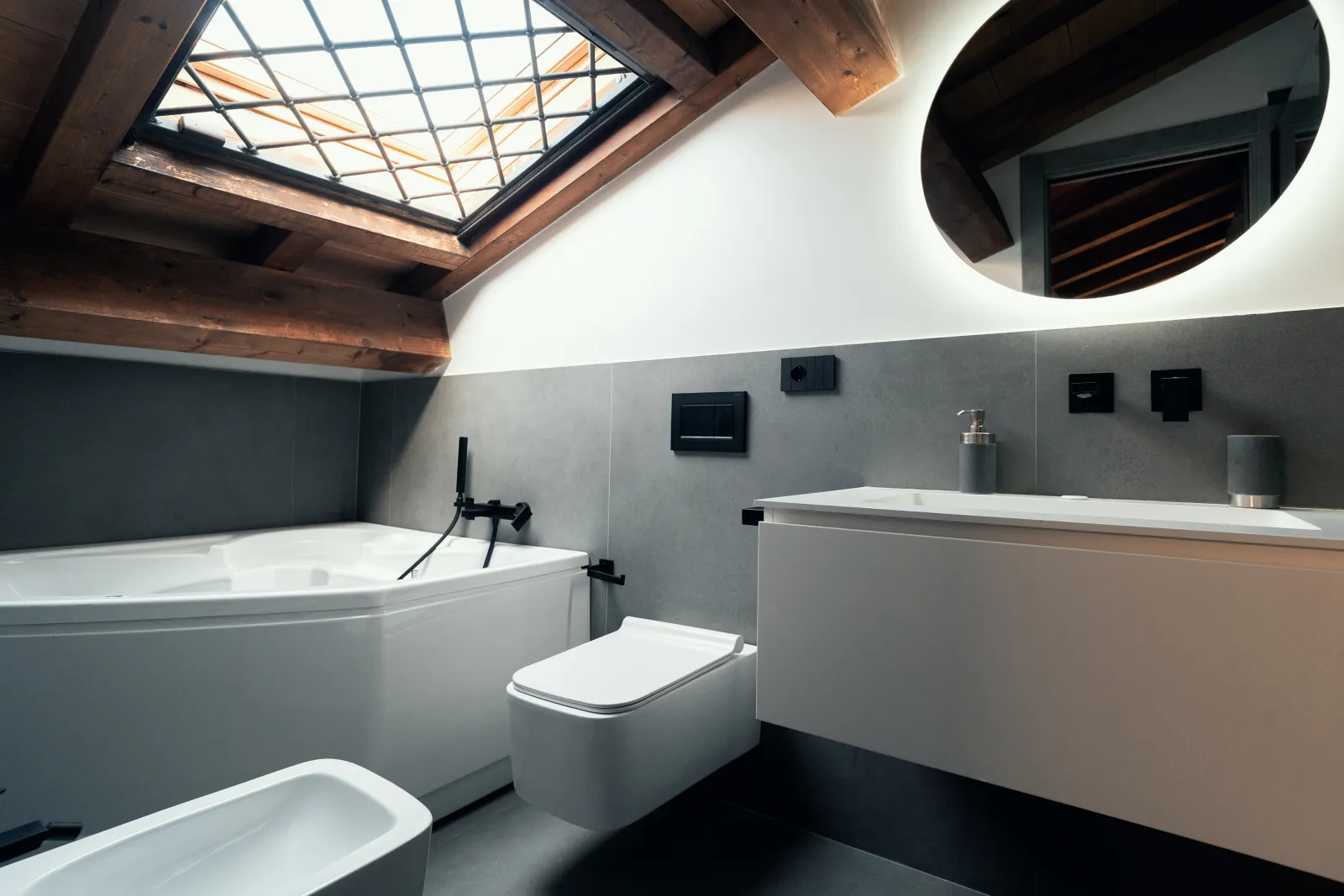 Bagno in mansarda con lucernario, vasca idromassaggio e rivestimento in grès grigio