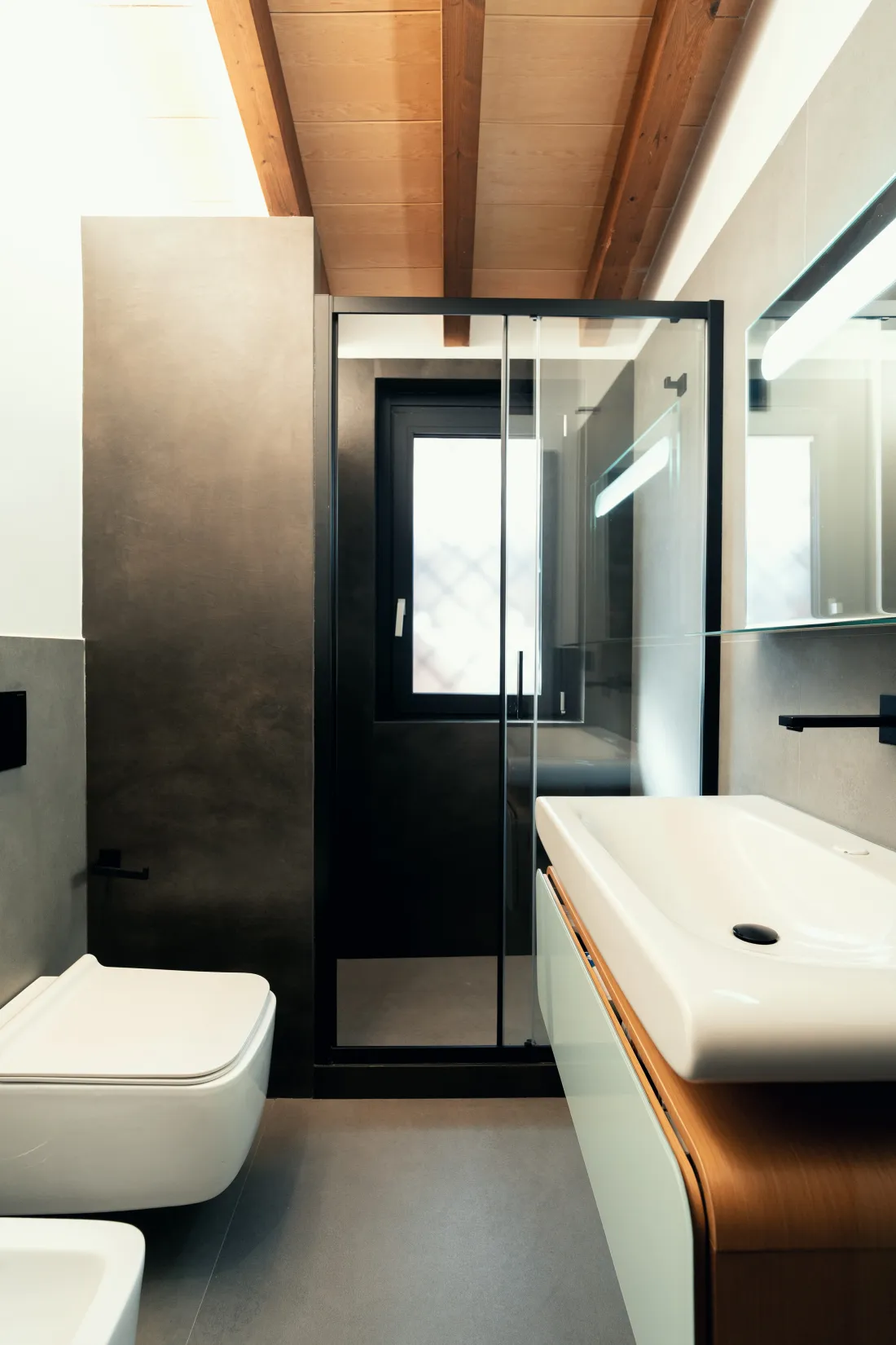Bagno con box doccia dal profilo nero, travi a vista e mobile curvo in legno