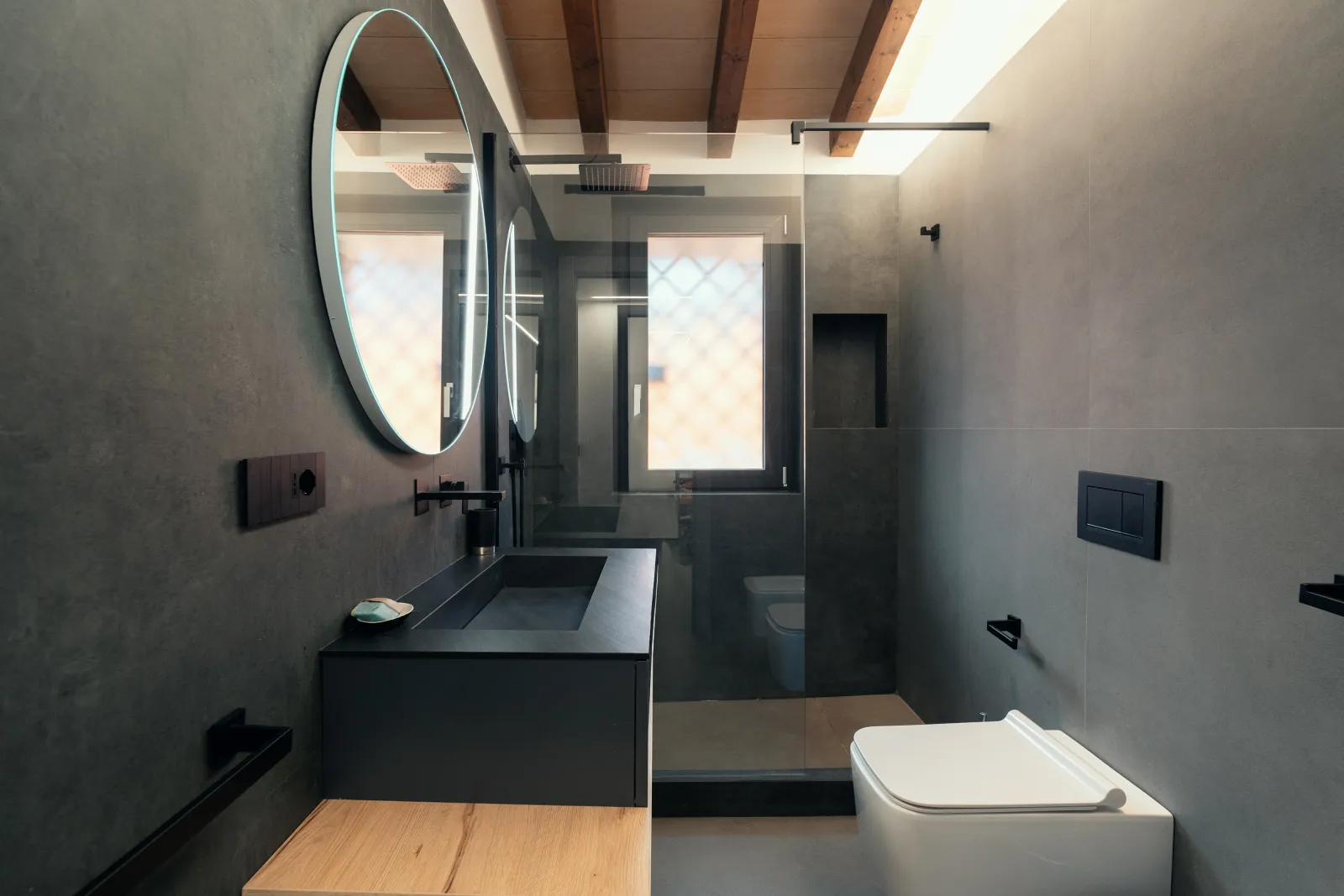 Bagno in grès grigio scuro con doccia walk-in, specchio tondo e seduta in legno